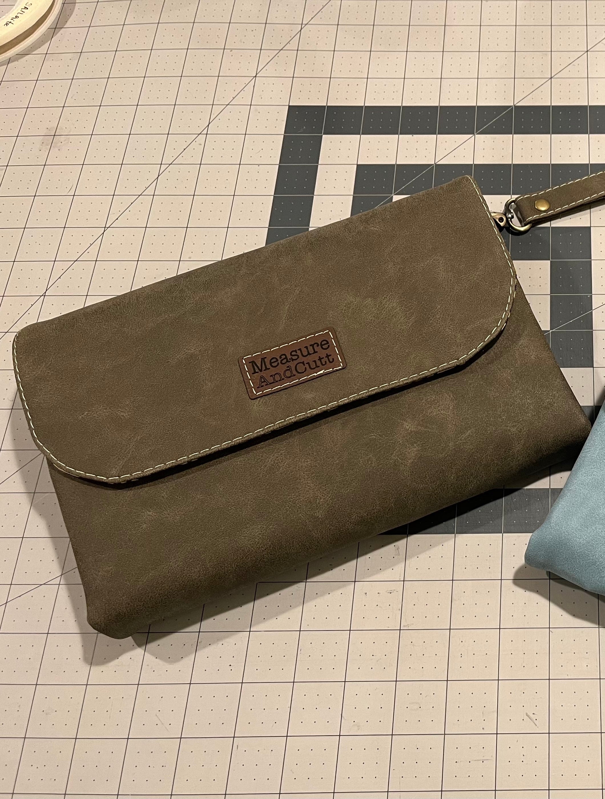 Measure and Cutt Brown clutch bag with a brand label on a cutting board surface