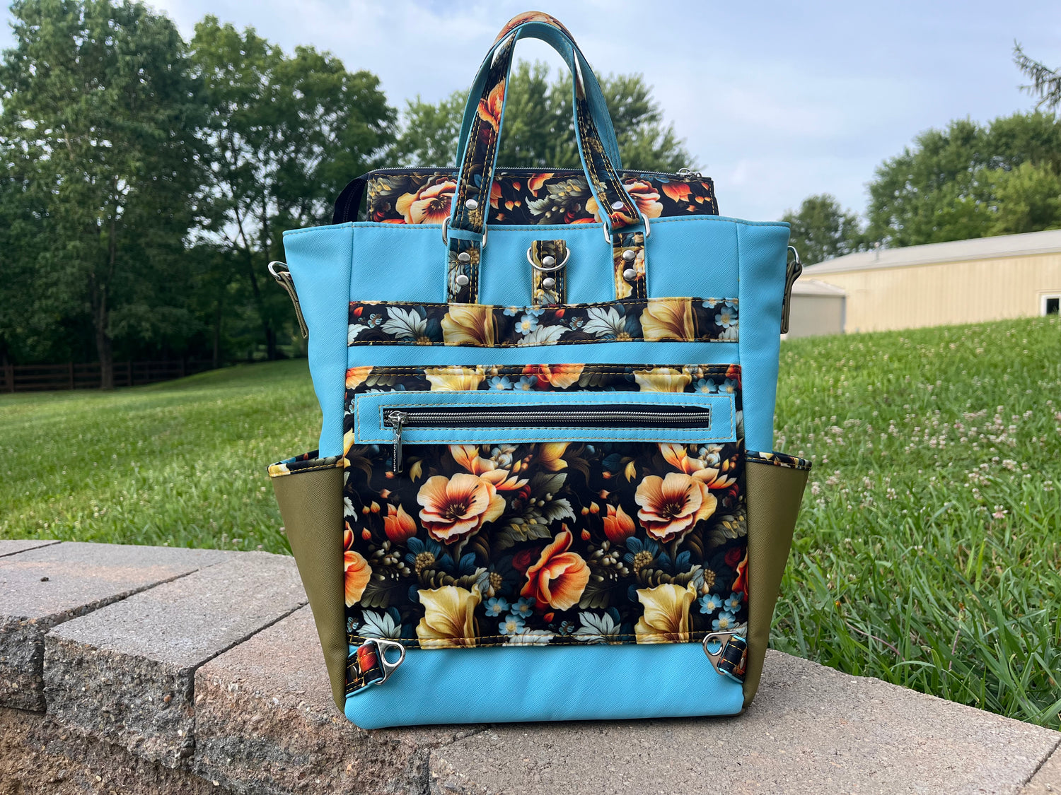 Measure and Cutt Floral-patterned backpack with blue accents on a stone ledge outdoors.