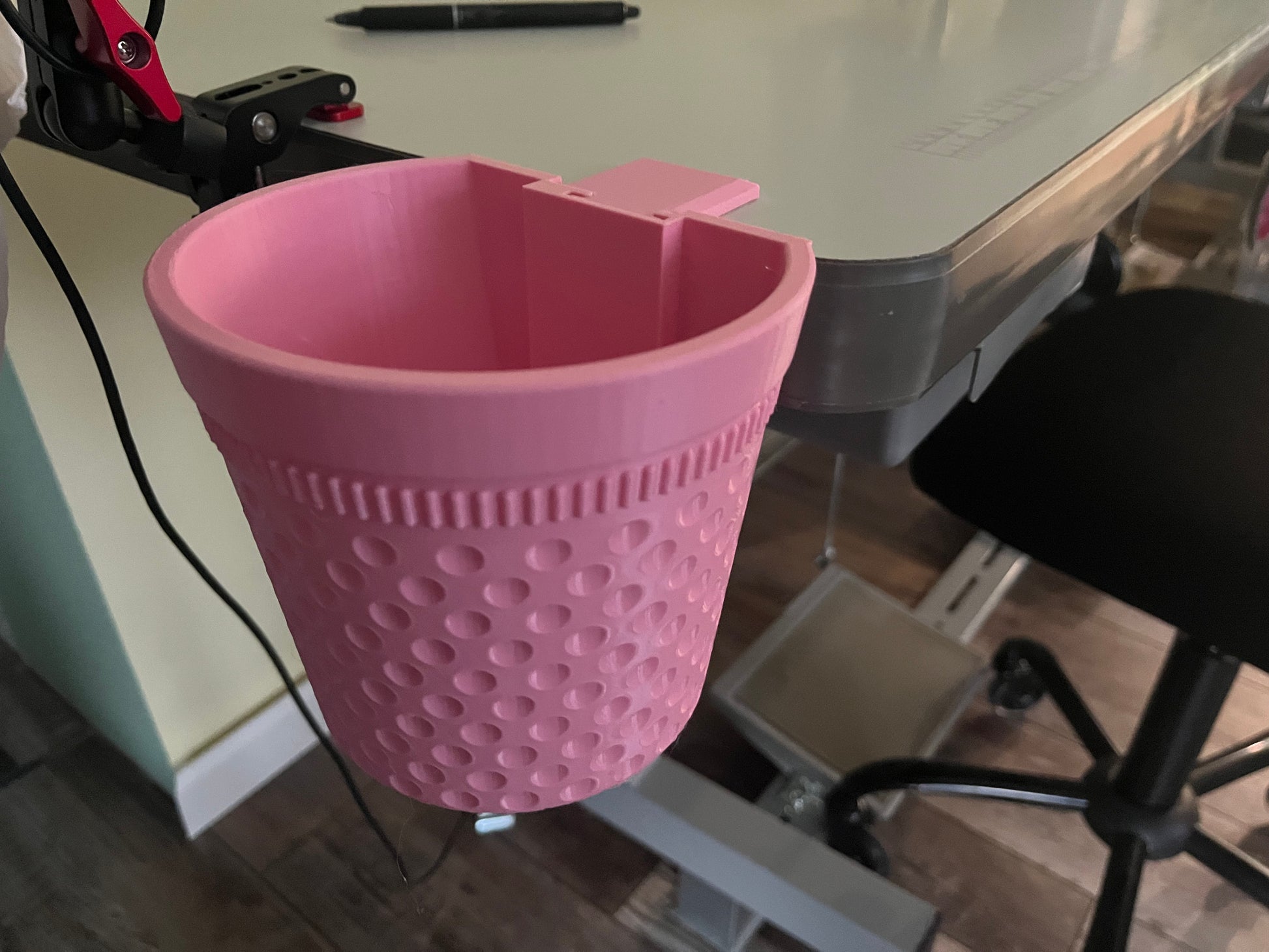 A pink thimble-shaped bin with table mount, attached to the edge of a table.
